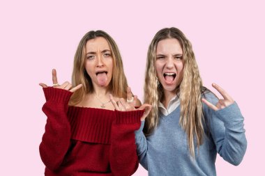 İki genç kadın pembe bir arka planda rock 'n roll hareketleri ve anlamlı yüzler yapıyor.