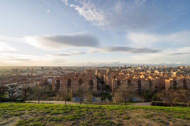 Batan güneşin sıcacık parıltısı yeşil bir tepe parkından görünen Madrid 'in manzarasını aydınlatıyor.