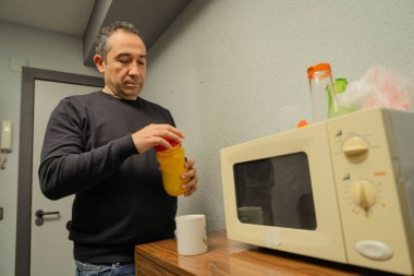 Sıradan bir ofis mutfağında ya da dinlenme odasında mikrodalganın yanında şişe açan bir adam.