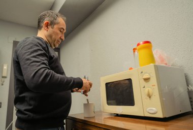 Adam mikrodalga fırının yanındaki bardakta sıcak bir içecek hazırlıyor.