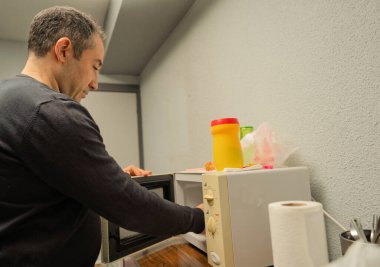 Adam modern bir mutfakta yemeğini ısıtmak için mikrodalga kapıyı açıyor.