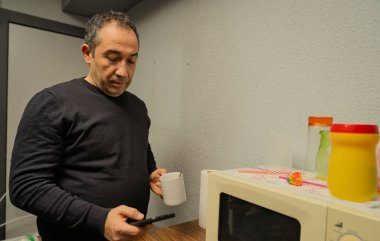 Ofis mutfağında mola verirken elinde kahve fincanı ve akıllı telefon tutan bir adam.