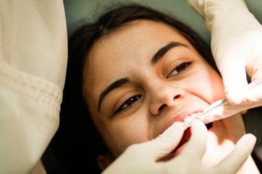 Bir ortodontist ziyareti sırasında gülümseyen hasta dişlerine seramik diş telleri taktırıyor.