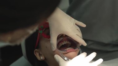 Profesyonel ortodontist genç bir hastanın ağzından plastik yanak çıkarıcıyı dikkatlice çıkarıyor.