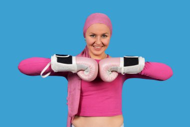 Pembe başörtüsü ve boks eldiveni takan gülümseyen kadın meme kanseri farkındalığını temsil ediyor.