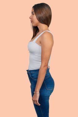 Profilde duran genç bir kadın, kot pantolon ve beyaz bir atlet giyiyor.