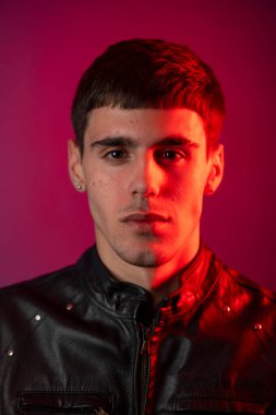 Siyah deri ceket giyen genç bir adamın stüdyo portresi. Kırmızı ve mor renkli dramatik bir ışıklandırma düzeniyle aydınlatılmış.