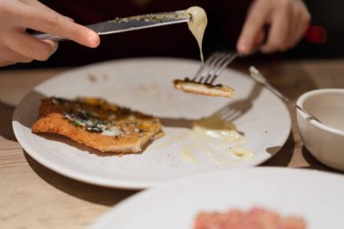 Peynir sosuna bulanmış lezzetli bir pirzola yemek için çatal ve bıçak kullanan eller.