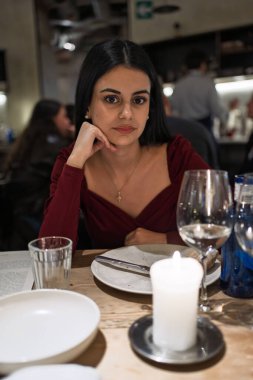 Genç bir kadın bir restoranda mum ve şarap bardağıyla masada oturuyor.