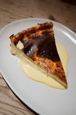 Beyaz tabakta muhallebi soslu peynirli kek dilimi.
