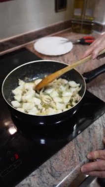 Gri saçlı yaşlı kadın sağlıklı bir yemek hazırlıyor ve tavada sebzeleri karıştırıyor.