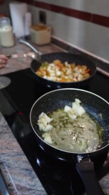 Gri saçlı yaşlı kadın sağlıklı bir yemek hazırlıyor ve tavada sebzeleri karıştırıyor.