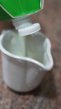 Taze inek sütü bir kutudan mutfak tezgahındaki beyaz seramik sürahiye dökülüyor.