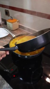 Buharı tüten sıcak suyu paella tavasına döken yaşlı bir kadın.