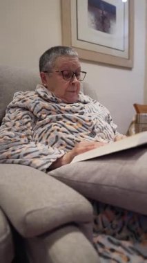 Yumuşak bir koltukta rahatça otururken gözlüklü rahat bir son sınıf kadınının romanının tadını çıkarması.