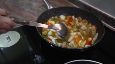 Son sınıf öğrencisi, tavukla sebzelerin rengarenk bir karışımını modern bir fırının tepsisinde karıştırıyor.