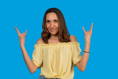 El hareketleriyle taş yapan ve mavi arka planda kameraya gülümseyen bir kadın.