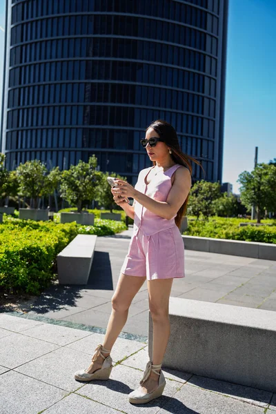 Modern şehir manzarasında akıllı telefondan mesaj atan genç bir kadın.