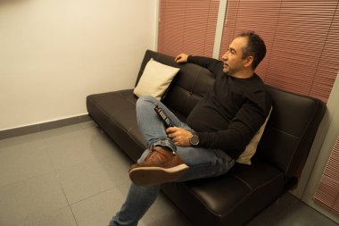 Televizyon izleyen ve evdeki kanepede dinlenen bir adam.