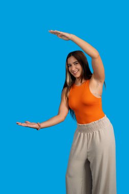 Mavi arka planda elleri arasında boşluk gösteren mutlu kadın.