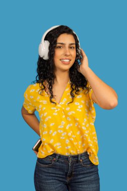 Sarı gömlek ve kulaklık takan gülümseyen kadın, ses içeriğini dinliyor.