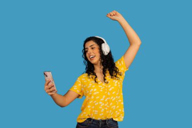 Kulaklık takmış, elinde telefonla mutlu bir şekilde dans eden genç bir kadın.