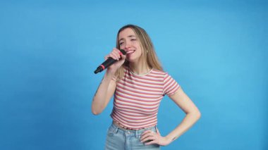 Tutkulu bir bayan şarkıcı, bir mikrofon kullanarak saf mavi bir arka plana şarkı söylüyor.