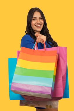 Başarılı perakende faaliyetlerinden sonra gülümseyen ve elinde birden fazla canlı alışveriş torbası tutan bir kadın.