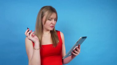 Kırmızı elbiseli genç kadın mavi arka planda bir stil ile dijital tablet üzerinde çizim yapıyor.