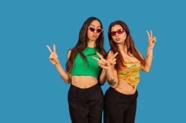 Genç kadınlar barış işareti yapıyor ve mavi arka planda dostluk gösteriyorlar.