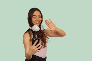 Kadın gülümsüyor, telefonu tutuyor ve video görüşmesi sırasında el sallıyor.