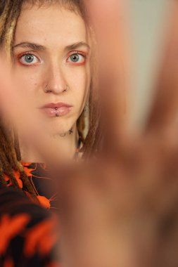 Rastalı ve piercingli genç bir kadın bir portre için poz veriyor, kameraya bakıyor.