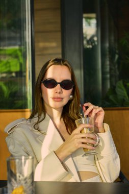 Güneş gözlüklü, buzlu kahve içen zarif bir kadın.