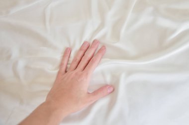Kadın eli nazikçe beyaz ipek çarşafa dokunuyor.
