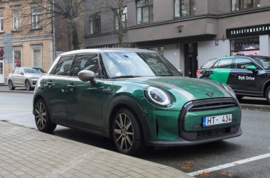 Riga, Letonya 01.22.2022 Küçük yeşil Mini Cooper şehir caddesine park etmiş. Fotoğraf, şehir mimarisi ve şehir atmosferine karşı arabayı ön plana çıkarıyor..