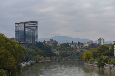 Kura Nehri üzerindeki bir köprüden panoramik manzara ve Tiflis, Gürcistan 'daki modern Radisson Blu oteli. Nehir, köprüler ve çağdaş mimariyle şehir manzarası.