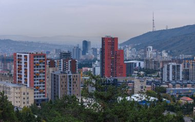 Tiflis 'in Saburtalo bölgesinin panoramik manzarası bir yamaçtan. Modern binalar, yerleşim alanları ve ufuktaki dağlar.