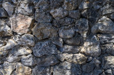 Güneş ışığıyla aydınlatılmış doğal bir taş duvara yakın çekim. Seyahat, tasarım ve inşaat projeleri için uygun desenli mimari arkaplan.