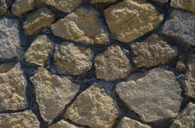 Parlak güneş ışığı altında sert, doğal bir taş duvara yakın çekim. Tasarım, reklam ve mimari projeleri için ideal desenli arka plan.