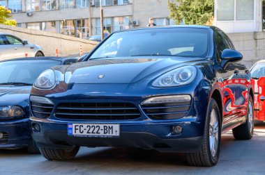 Tiflis, Gürcistan, 10.29.2025. Siyah Porsche SUV konut binasının yakınına park edilmiş. Kentsel geçmişe sahip modern bir araba..