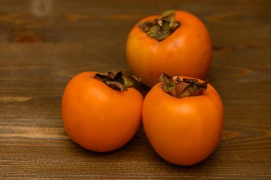 Tahta bir masada taze ve olgun hurma meyveleri. Parlak turuncu renk ve yumuşak doku meyvelerin tazeliğini ve doğal güzelliğini vurgular. Sağlıklı gıda kavramı, mevsimlik meyveler