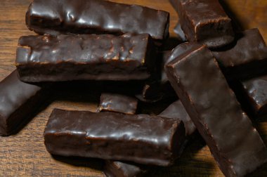 Tahta bir yüzeyde duran çikolatalı şekerler ve çubuklar. Kahverengi tonda tatlı, üst manzara, doğal ışık.