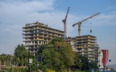 Tiflis, Gürcistan 'da modern bir gökdelen inşaatı. İki kule vinç, açık mavi gökyüzüne karşı malzeme kaldırıyor. Kentsel kalkınma ve şehir altyapı büyümesi kaydedildi.