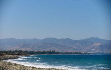 Kıbrıs 'taki Akdeniz' in sakin turkuvaz suları ve uzak dağlarıyla panoramik manzarası seyahat, doğa ve kıyı fotoğrafçılığı için mükemmel. Kıbrıs 'ta deniz ve arka planda dağlar. Yüksek kalite fotoğraf