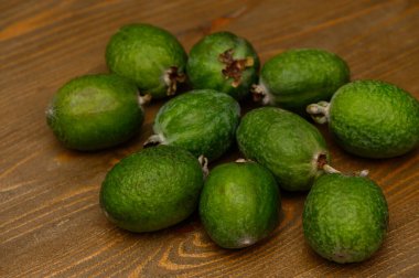 Tahta bir masada duran taze yeşil feijoa meyveleri. Doğal ışık, tropikal meyvelerin dokusunu ve zengin rengini ön plana çıkarır. Sağlıklı beslenme, organik yaşam tarzı ve doğal gıda kavramı.