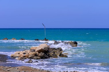 Kıbrıs kıyısı yakınlarında denizde duran fenerli taştan dalgalı su. Sakin dalgalar, berrak gökyüzü, huzurlu Akdeniz manzarası.