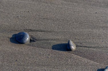 Deniz taşları ve çakıl taşları, sakin bir yaz manzarası yaratan yumuşak Akdeniz dalgaları ve güneşli gökyüzü ile bir Kıbrıs plajının kumlu sahillerine saçılmış..