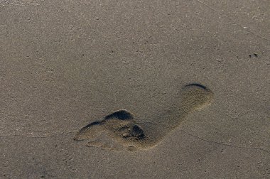 Kıbrıs plajında altın bir kuma bastırılmış erkek ayak izinin yakın planında, arka planda yumuşak Akdeniz dalgaları var.