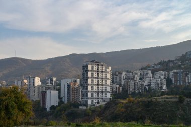 Oranın ruhunu yansıtan sarsıcı bir çekim. Çocuk parkları, park edilmiş arabalar, zemin katlardaki dükkanlar, sakinler, tipik bir Tiflis bölgesinde canlı, gürültülü ve otantik bir ortam yaratan her şey.. 