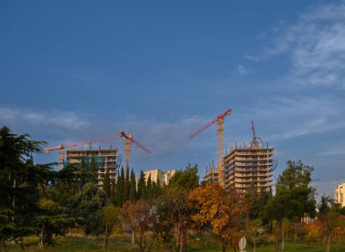 Büyüyen bir şehrin güçlü silueti. İki uzun vinç, uçsuz bucaksız gökyüzünün altında müstakbel bir yerleşim yerinin çelik ve beton iskeletinin üzerinde yükseliyor. Geliştirme sembolü.